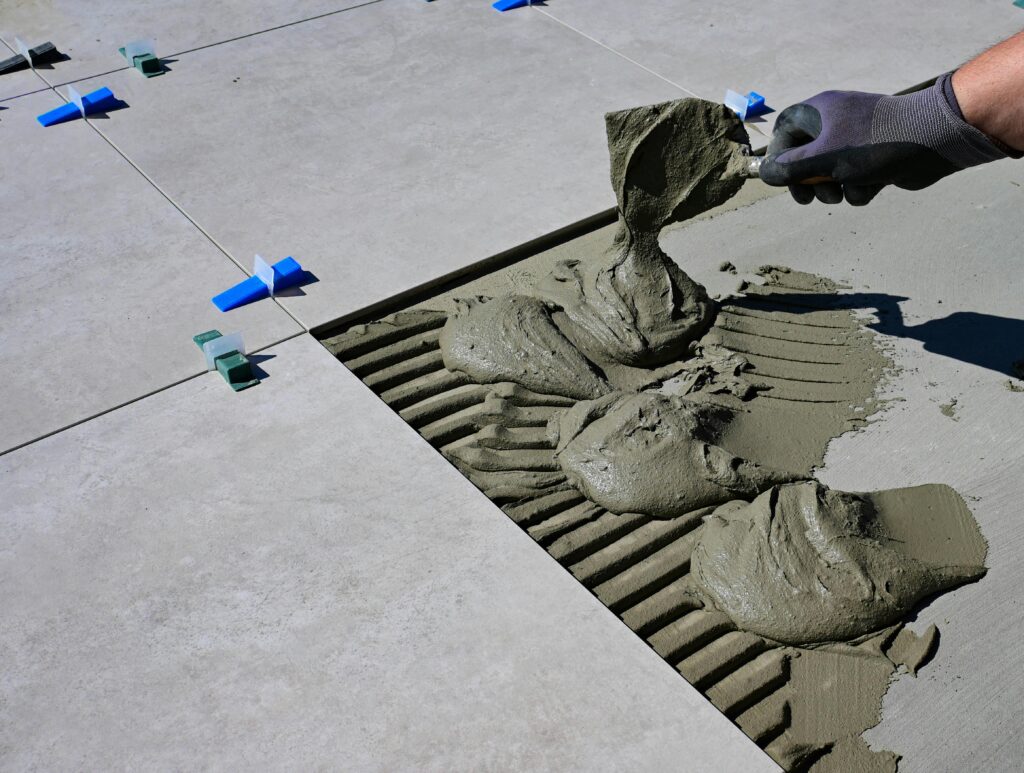 Close-up of a gloved hand applying mortar for ceramic tile installation outdoors.