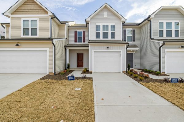 Contemporary suburban homes with garages and neat lawns under a clear sky.