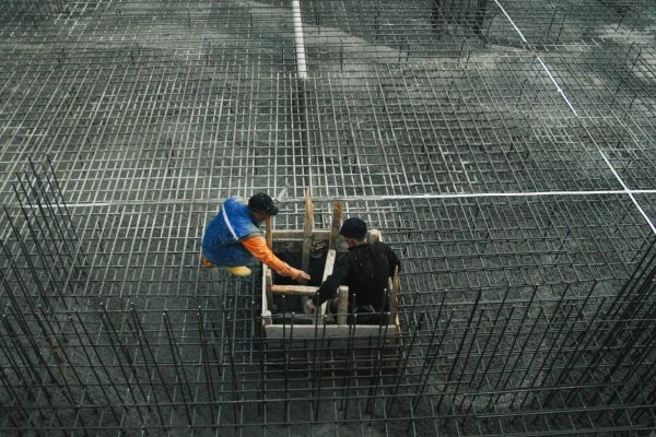 Two workers operating on a construction site with steel frameworks and concrete. High-angle view captures teamwork and industry.